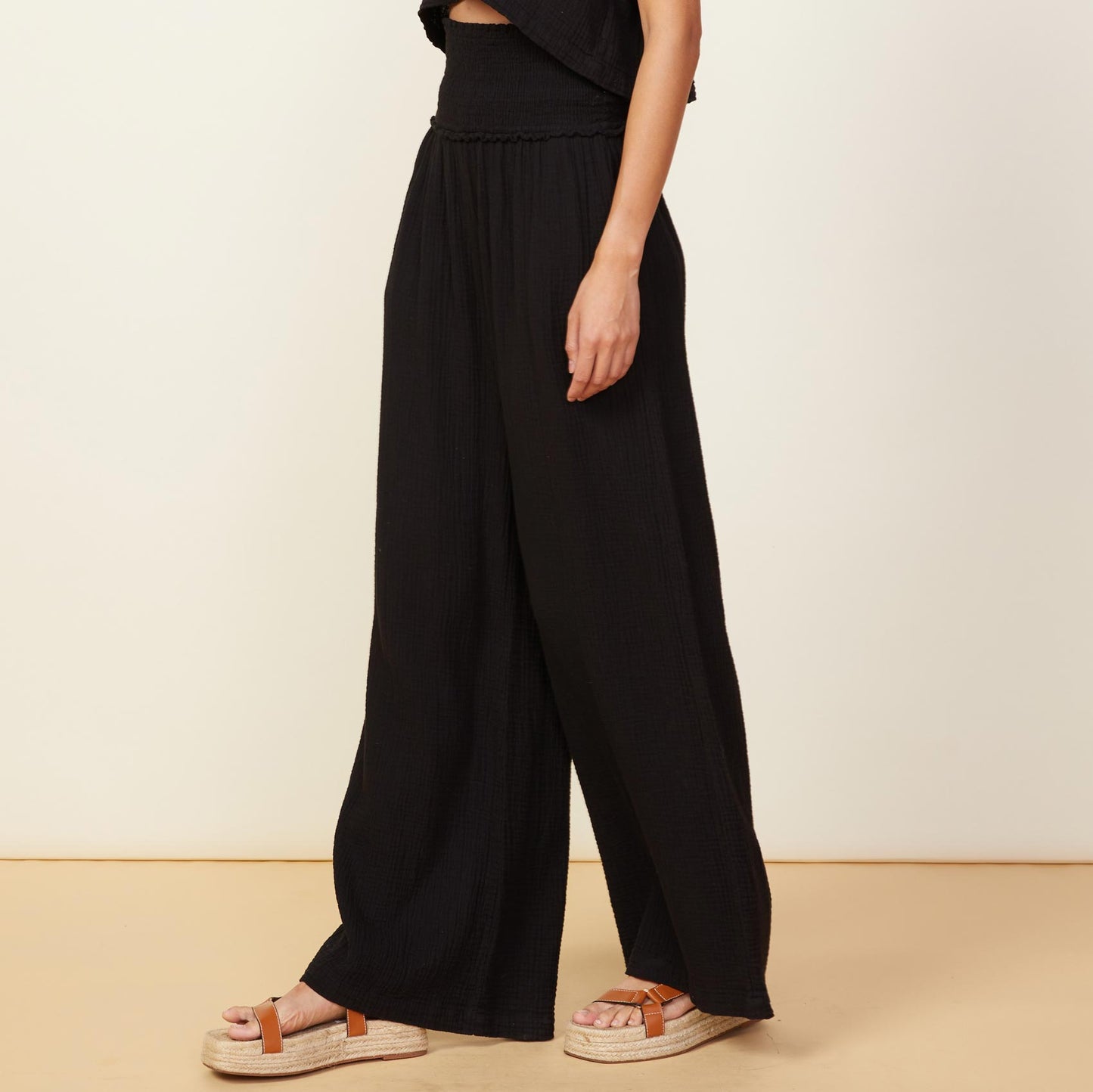 Side view of model wearing the gauze smocked flare pant in black.