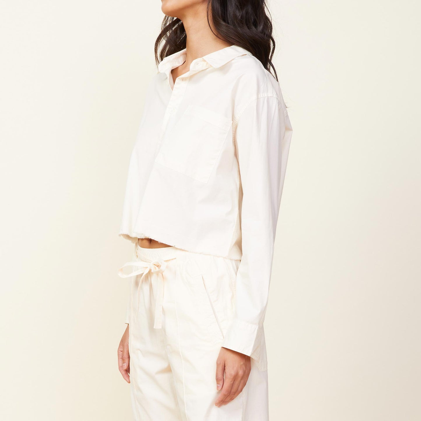 Side view of model wearing the cropped poplin shirt in off white.