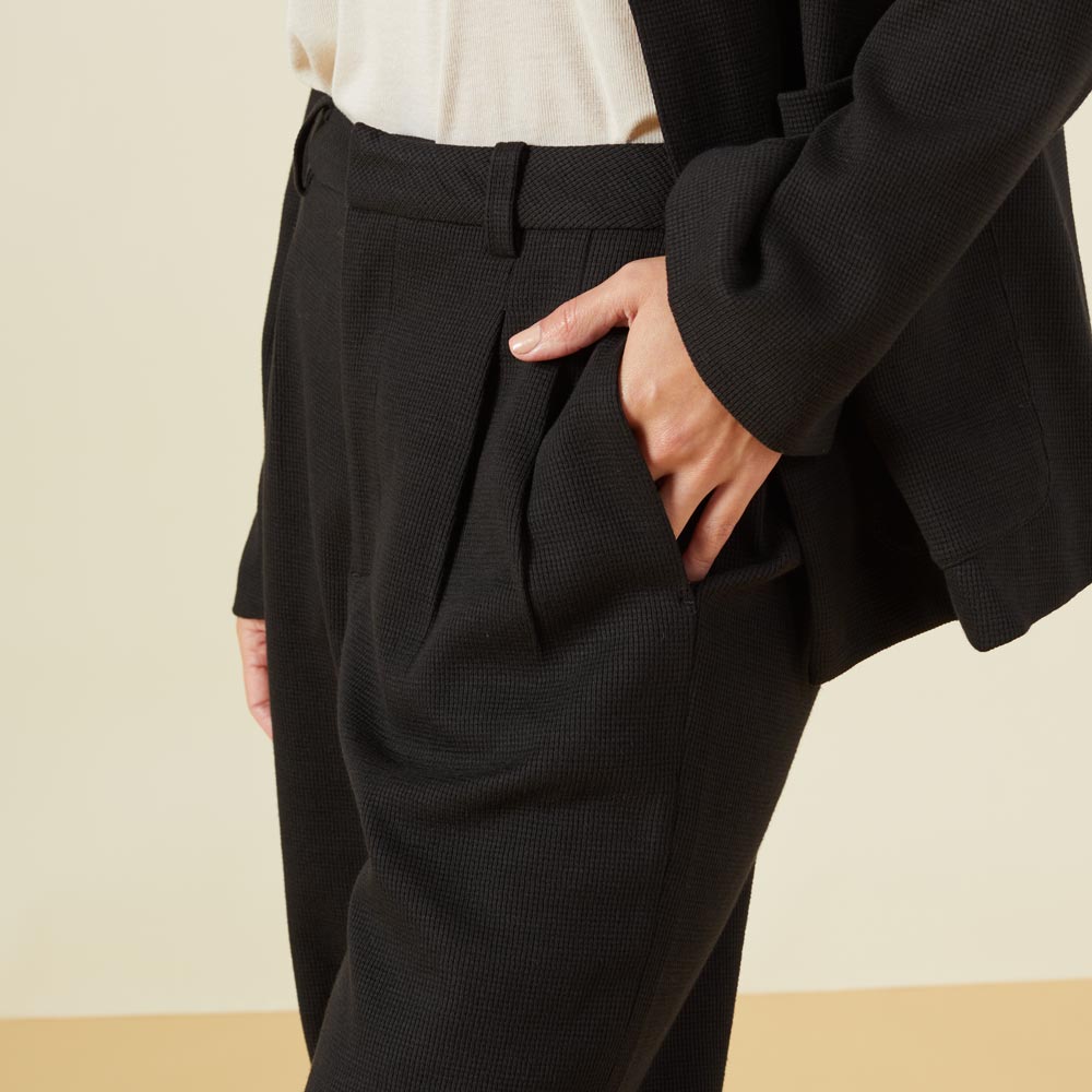 Close up view of model wearing the bonded thermal pleated pants in black.