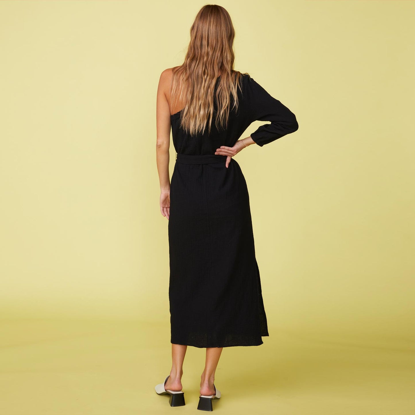 Back view of a model wearing the gauze one shoulder dress in black.
