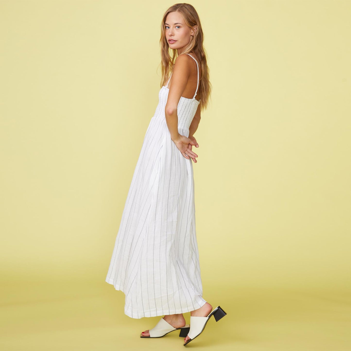 Side view of model wearing the pinstripe gauze smocked maxi dress in white.