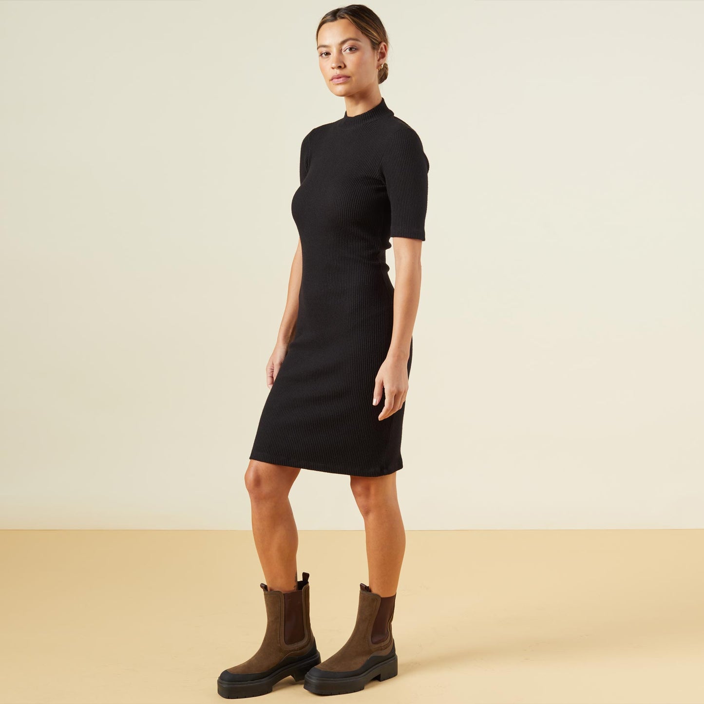 Side view of model wearing the brushed rib mock neck dress in black.
