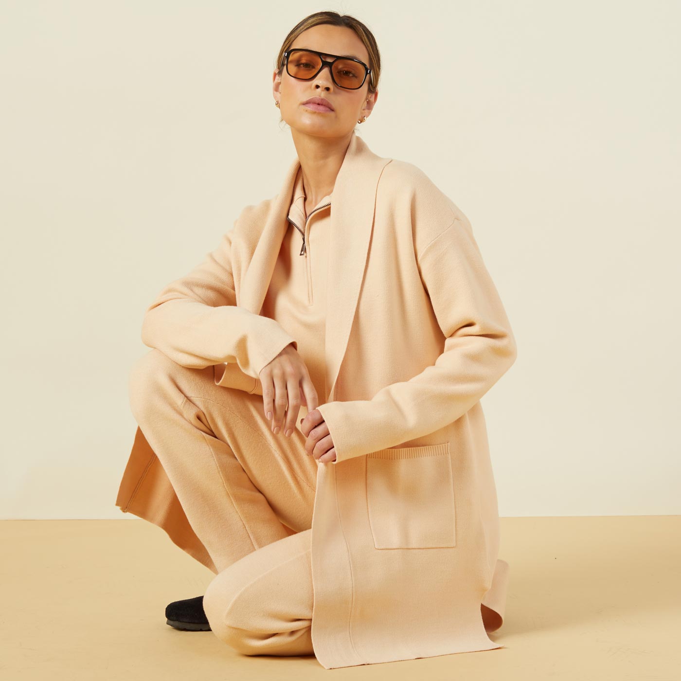 Front view of model kneeling while wearing the supersoft sweater knit cardigan in vanilla.