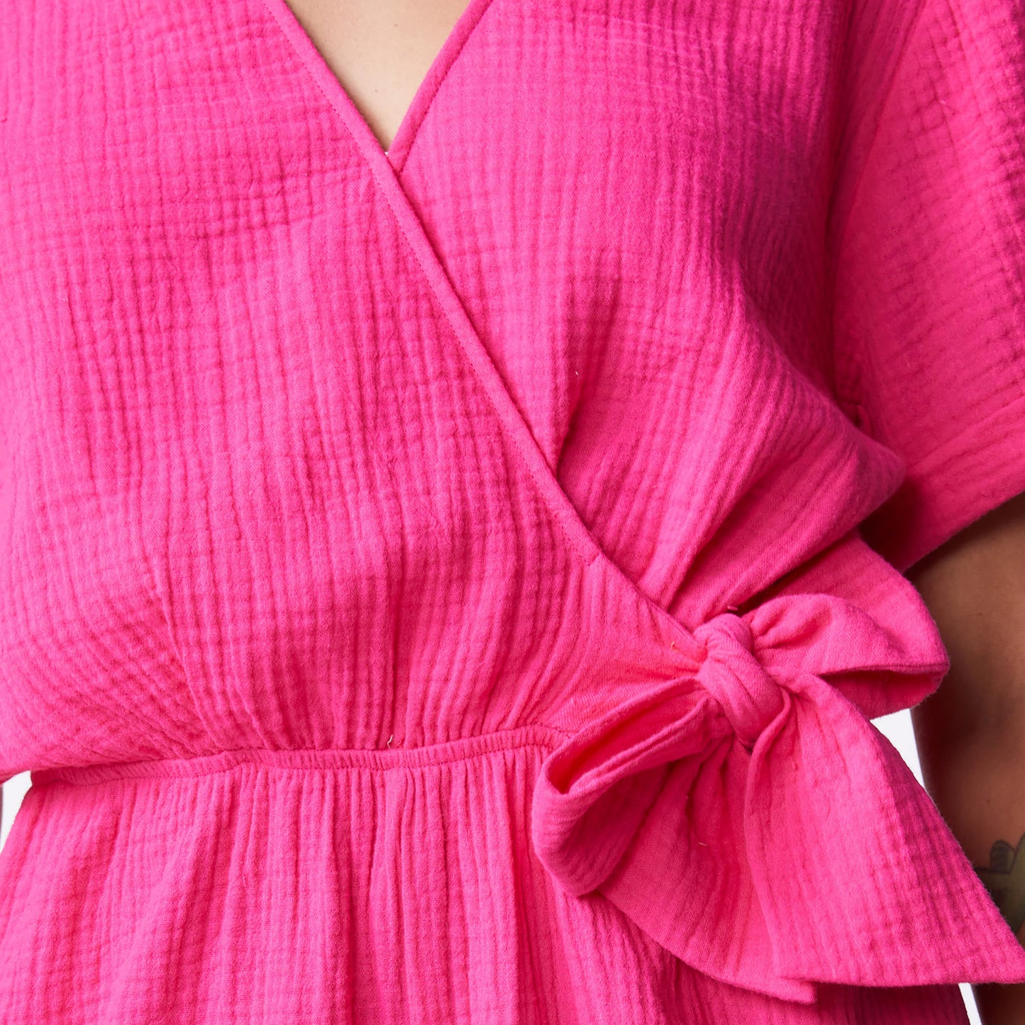 Close up detail of bow tie on the gauze wrap romper in raspberry.