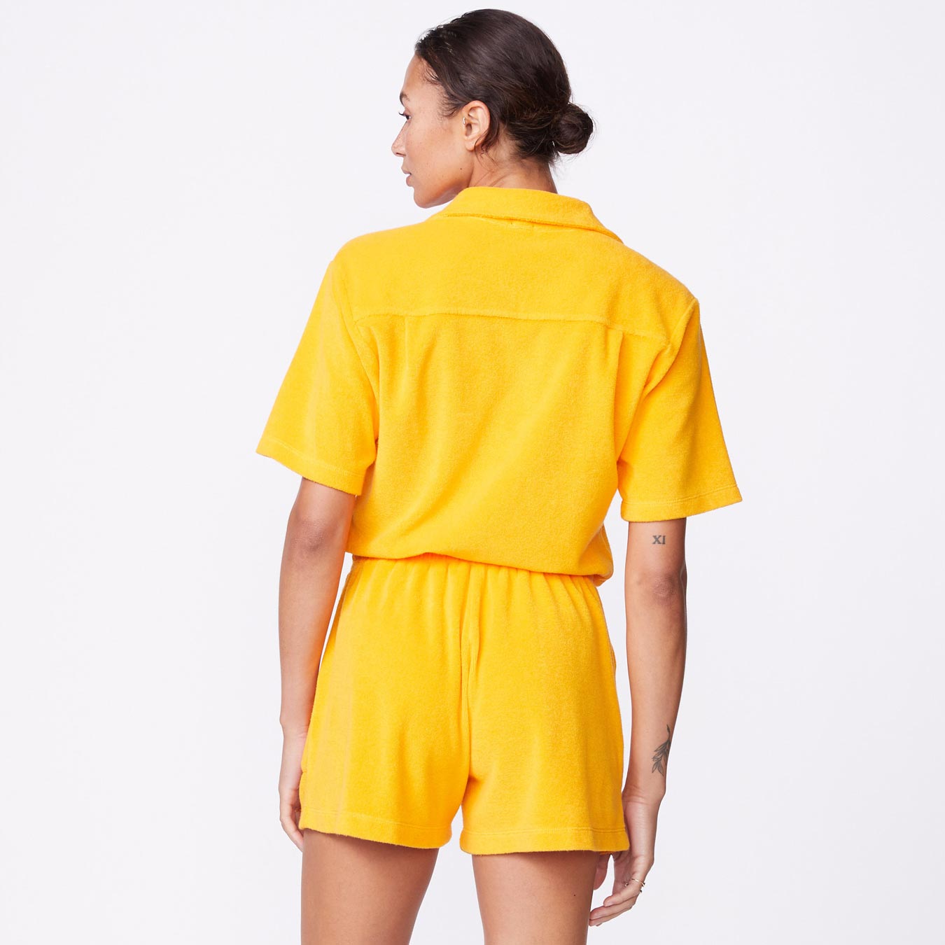 Back view of model wearing the terry cloth romper in marigold.
