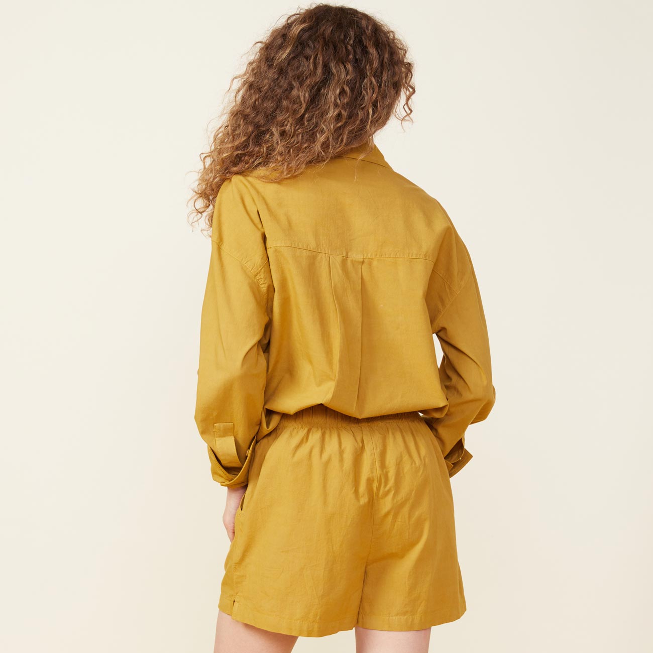 Back view of model wearing the poplin shirt in golden olive.