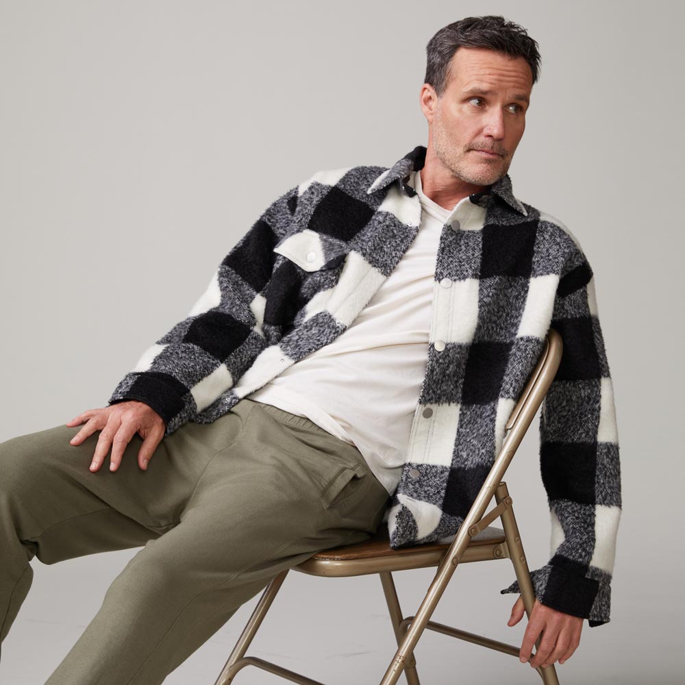 Front view of model sitting in chair wearing the plaid flannel jacket in black, natural check.
