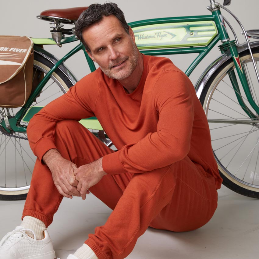 Front view of model wearing the lounge sweatshirt in faded rust sitting in front of a bike.